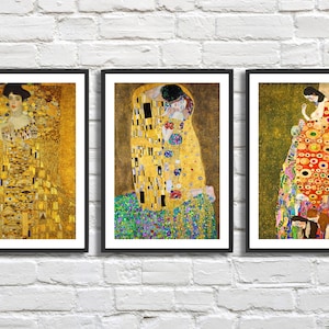 Op de afbeelding: Drie ingelijste kunstprints met schilderijen van Gustav Klimt. De prints zijn in zwarte lijsten en hebben een gouden achtergrond met kleurrijke figuren en patronen.