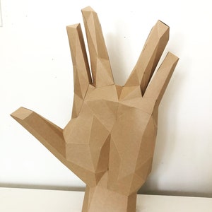 May include: A brown paper hand sculpture with a geometric design. The hand is in a raised position with the fingers spread apart.