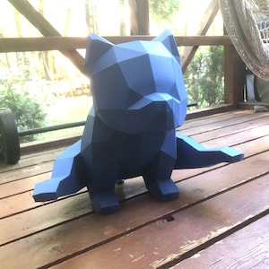 May include: A blue, geometric, origami-style sculpture of a dog sitting on a wooden surface.