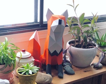 Puede incluir: Una escultura de papel de un zorro de color naranja y gris, de pie sobre una mesa de madera con plantas en macetas. El zorro tiene una cola larga y tupida y un hocico puntiagudo.
