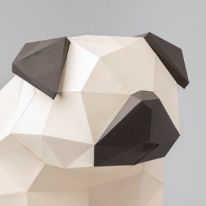 Op de afbeelding: Een wit en zwart papieren model van een mopshond. Het model is gemaakt van gevouwen papier en heeft een geometrisch ontwerp.