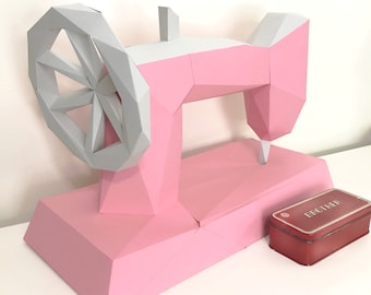 May include: A pink and gray papercraft model of a sewing machine with a Brother sewing box. The sewing machine has a large wheel and a needle.