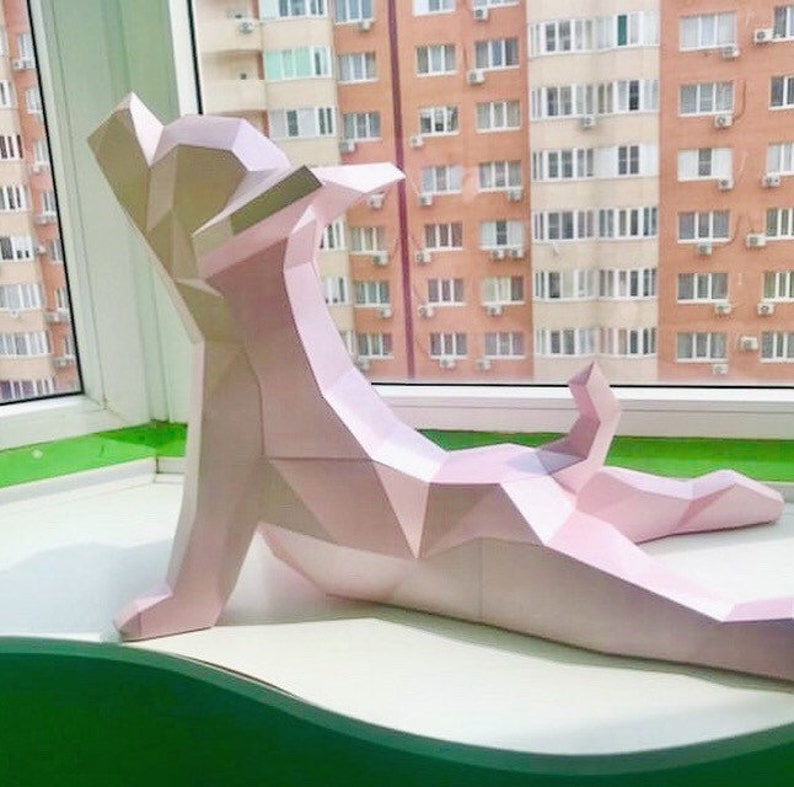 May include: A pink papercraft model of a dog lying down on a windowsill. The dog is made of folded paper and has a geometric design.