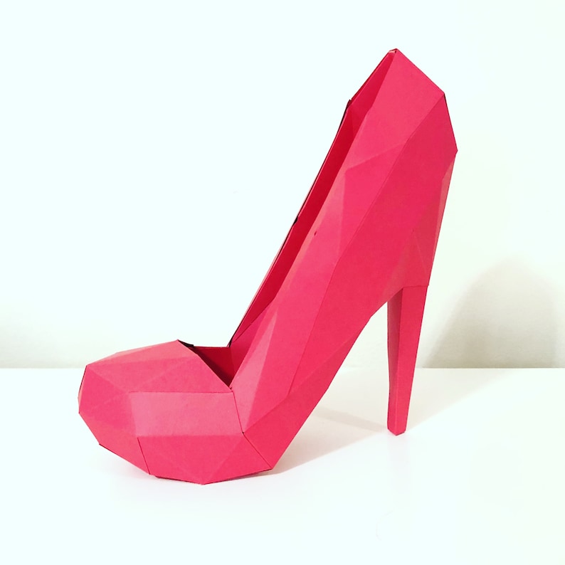 May include: A vibrant pink high-heeled shoe with a geometric, faceted design. The shoe features a pointed toe, a slender heel, and a platform sole. The overall aesthetic is modern and artistic.