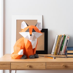 May include: A papercraft fox sculpture in orange, white, and black colors. The fox is sitting on a wooden table with books and pencils in the background.