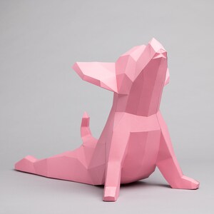 May include: A pink papercraft chihuahua sculpture in a yoga pose, with its head tilted back and its legs stretched out.