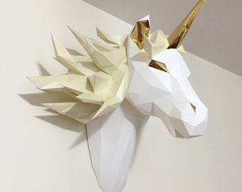 May include: A white papercraft unicorn head with a gold horn and mane. The unicorn is mounted on a white wall.