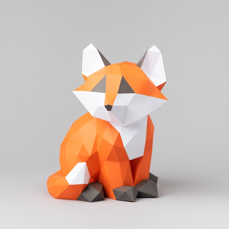 May include: A papercraft fox figurine in orange, white, and gray. The fox is sitting with its head tilted to the side and its tail curled behind it.