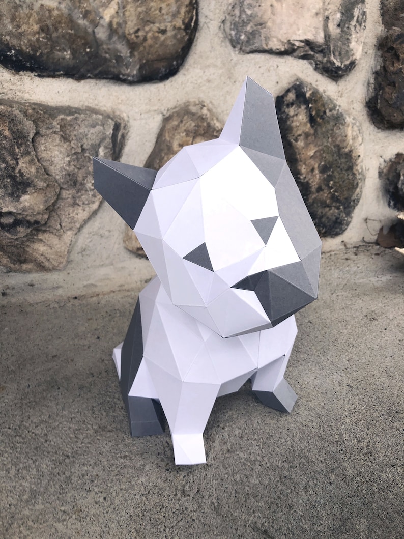 May include: A white and grey papercraft model of a sitting bulldog. The model is made of folded paper and has a geometric design.