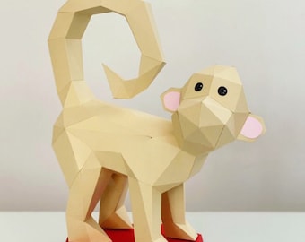 May include: A beige papercraft monkey with a curled tail, pink ears, and black eyes. The monkey is standing on a red and blue platform.