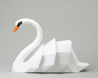 May include: A white paper swan sculpture with an orange beak and black eyes. The swan is folded into a geometric shape.