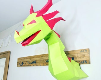 May include: A green and red paper dragon sculpture with a long neck and a wide mouth. The dragon is mounted on a wall with a wooden ruler underneath.