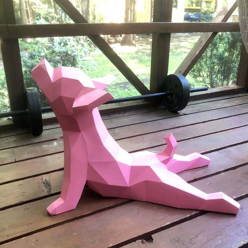 May include: A pink origami paper dog sculpture in a yoga pose. The dog is made of folded paper and has a geometric design.