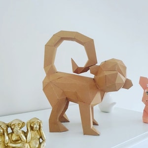 May include: A brown geometric paper monkey sculpture. The monkey has a curled tail and is standing on all fours. The sculpture is made of folded paper with a polygonal design. Other decorative items are in the background, including a gold monkey statue.