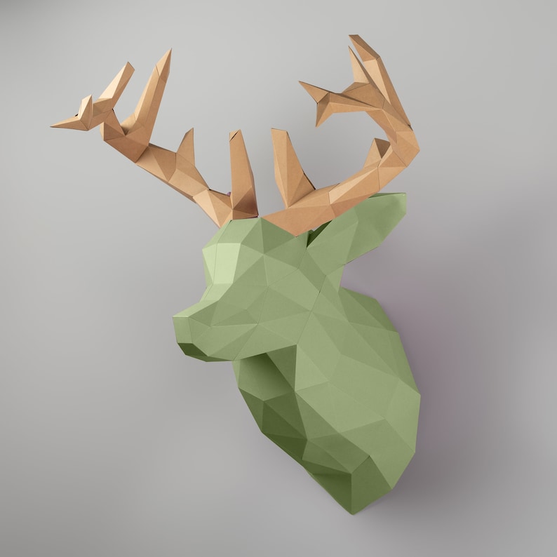May include: A green papercraft deer head with brown paper antlers. The deer head is made of folded paper and has a geometric design.