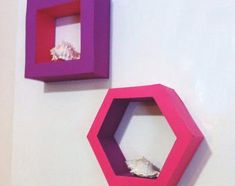 May include: Two wall-mounted shelves in a square and hexagonal shape. The square shelf is purple with a red interior, and the hexagonal shelf is pink with a purple interior. Each shelf contains a seashell.