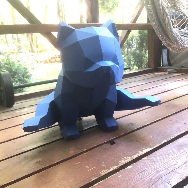 May include: A blue, geometric, origami-style sculpture of a dog sitting on a wooden surface.
