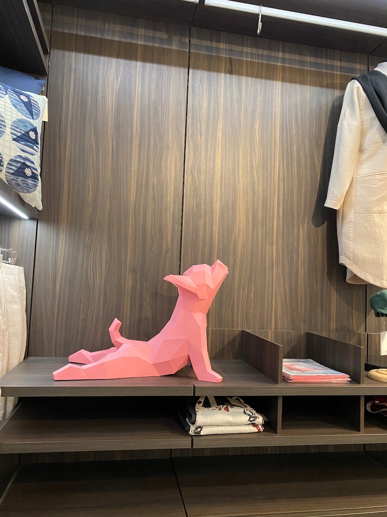 May include: A pink origami-style dog sculpture on a shelf in a closet. The dog is in a yoga pose with its legs stretched out and its head tilted back.