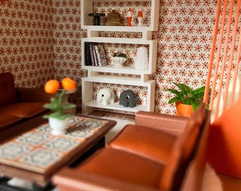 May include: A miniature mid-century modern living room scene. The room features a white bookshelf with decorative items, a brown sofa, a coffee table, and a patterned wallpaper. A painting hangs on the wall. The scene is decorated with orange and brown tones.