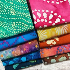 May include: A stack of 10 fabric squares with various colorful batik patterns. The fabrics feature a variety of designs, including dots, swirls, and abstract shapes. The fabrics are arranged in a staggered pattern, with the top fabric being a bright pink with white dots.