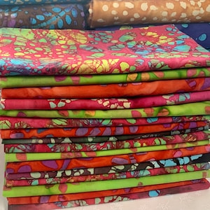 May include: A stack of colorful fabric napkins with a batik pattern. The napkins are folded and stacked neatly, with the top napkin showing a bright red background with green, blue, and yellow accents.