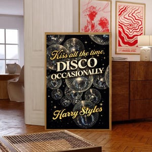 May include: A framed art print with a black background and gold text that reads "Kiss all the time, DISCO OCCASIONALLY Harry Styles." The print features multiple disco balls. Two other framed prints are visible in the background.