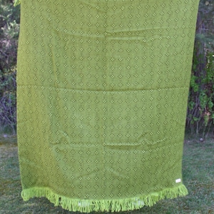 May include: A green blanket with a repeating diamond pattern and fringe trim. The blanket is a vibrant shade of green and appears to be made of a soft material. The fringe is a lighter shade of green.