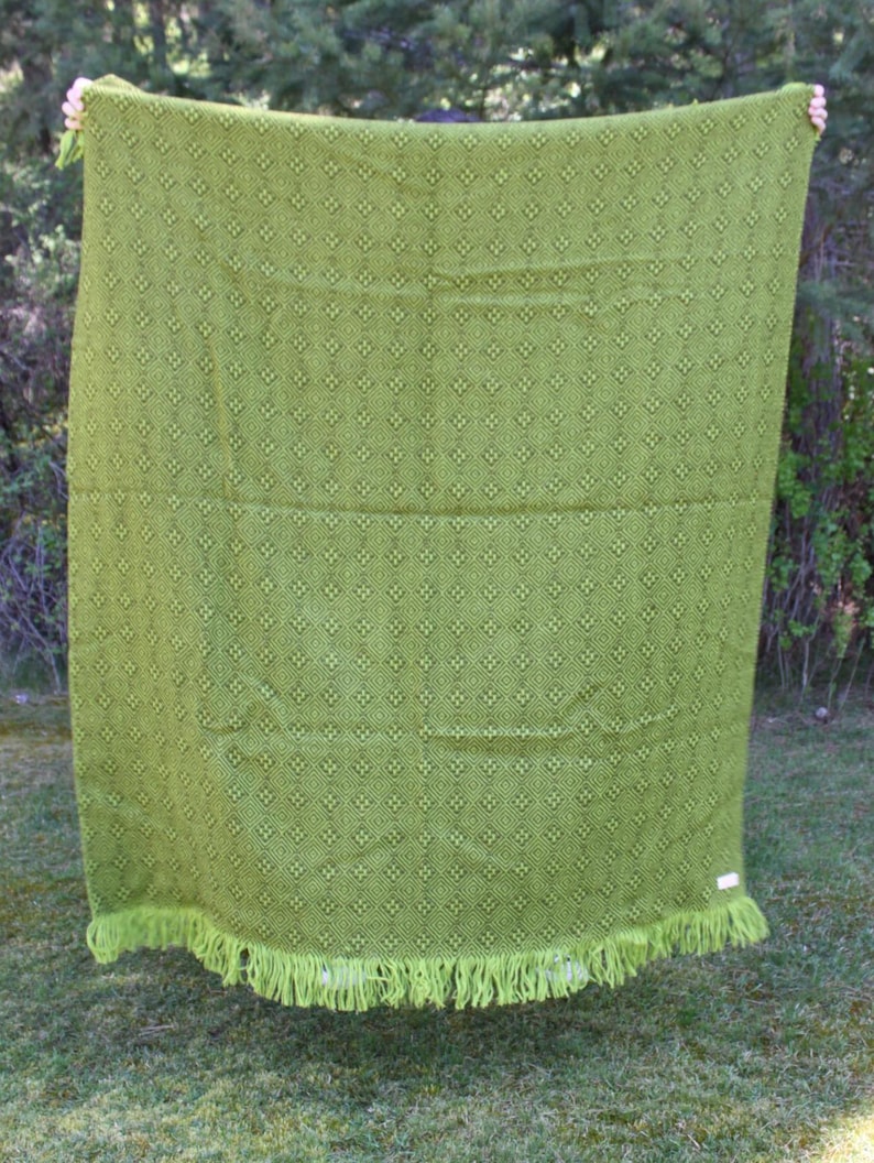 May include: A green blanket with a repeating diamond pattern and fringe trim. The blanket is a vibrant shade of green and appears to be made of a soft material. The fringe is a lighter shade of green.