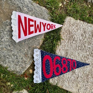 May include: Two pennant flags with white lace trim. One is white with red polka dots and the word "NEW YORK" in red. The other is navy blue with white polka dots and the numbers "06870" in red.