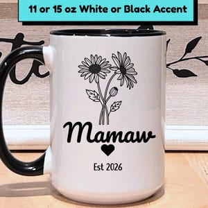 May include: White ceramic mug with a black handle and rim. The mug features a floral design with the word "Mamaw" and a heart, along with "Est 2026". The mug is available in 11 or 15 oz sizes.