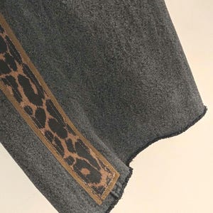May include: A section of gray fabric with a diagonal brown and black leopard print accent. The fabric has a textured appearance and a raw, unfinished edge.