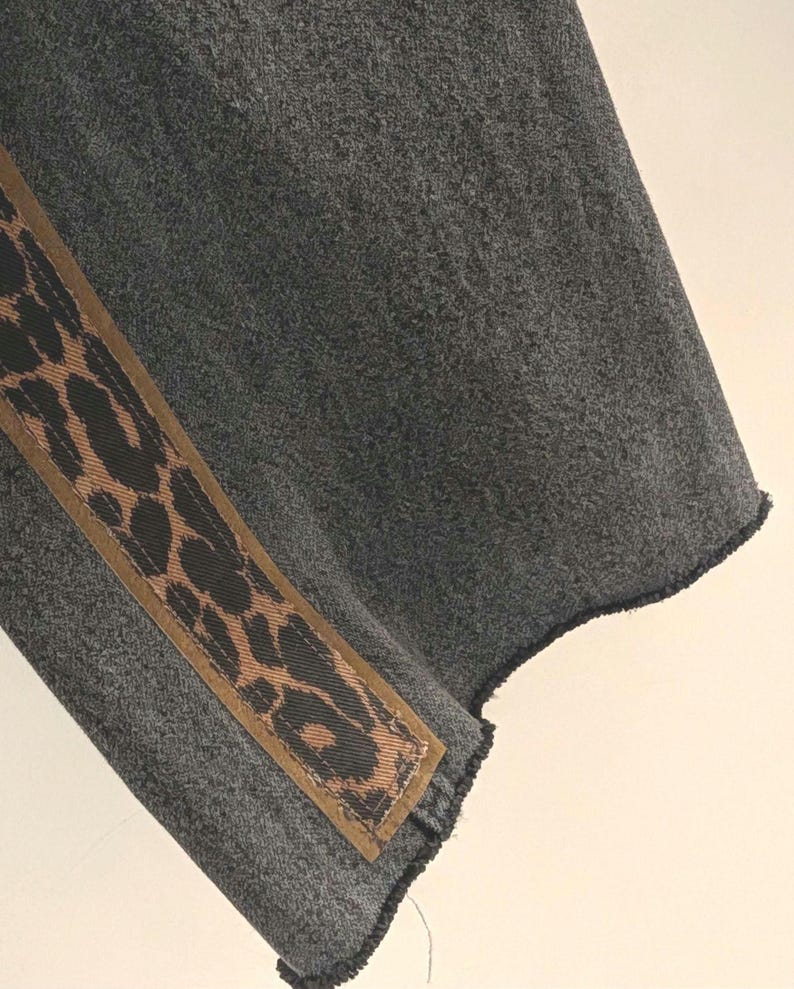 May include: A section of gray fabric with a diagonal brown and black leopard print accent. The fabric has a textured appearance and a raw, unfinished edge.