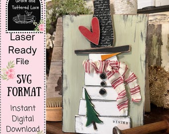 May include: A wooden snowman decoration with a red heart, black hat, and striped scarf. The snowman has three black button eyes and a green tree. The word "WINTER" is at the bottom. The image also includes text that says "Grace and Tattered Lace", "Laser Ready File", "SVG FORMAT", and "Instant Digital Download".