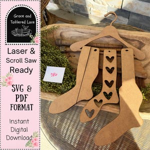 May include: Laser-cut wooden sock cutouts, including one with heart-shaped cutouts, displayed on a wooden hanger. The image includes the text "Laser & Scroll Saw Ready" and "SVG & PDF FORMAT". A small note reads "386".