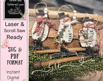 May include: Three wooden snowman ornaments with black top hats, carrot noses, and red and white accents. Each snowman has a unique design, including a snowflake, a Christmas tree, and a candy cane. The ornaments are ready for laser and scroll saw projects.