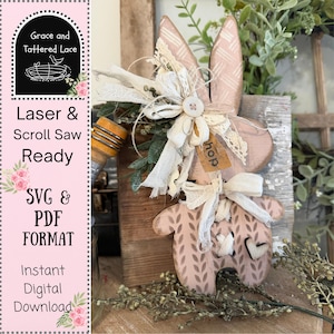 May include: A wooden Easter bunny decoration with a pink and white patterned design. The bunny has large ears, a bow, and a small tag that says "hop". The image also includes the text "Laser & Scroll Saw Ready" and "SVG & PDF FORMAT".