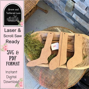 May include: Four unfinished wooden sock cutouts, displayed on a wooden tray with greenery. The socks are various shapes and sizes, ready for laser or scroll saw projects. The image includes text that says "Laser & Scroll Saw Ready" and "SVG & PDF FORMAT".