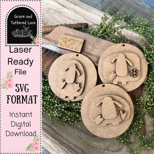 May include: Laser-ready SVG file featuring layered wooden penguin ornaments. The ornaments are laser cut from light brown wood and include a small tag. The image also includes the text "Grace and Tattered Lace", "Laser Ready File", "SVG Format", and "Instant Digital Download".