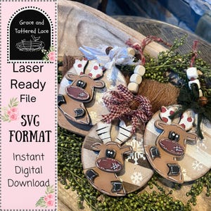 May include: Three wooden reindeer ornaments with brown and white antlers, red noses, and black accents. The ornaments are round and decorated with snowflakes. The image also includes the text "Laser Ready File SVG FORMAT Instant Digital Download."