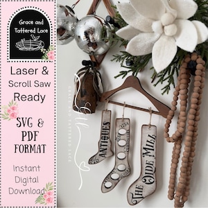 May include: A wooden hanger displays three decorative sock-shaped ornaments with the words "ANTIQUES", "1754 CURIOSITIES", and "THE OIDE MILL" printed on them. The image also includes a pink background with text that reads "Laser & Scroll Saw Ready SVG & PDF FORMAT Instant Digital Download".