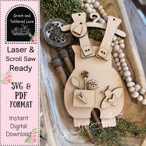 May include: A wooden cutout of dungarees with decorative elements, including a pocket with flowers and a butterfly. The overalls are designed for laser and scroll saw projects, with the text "Laser & Scroll Saw Ready" and "SVG & PDF FORMAT".