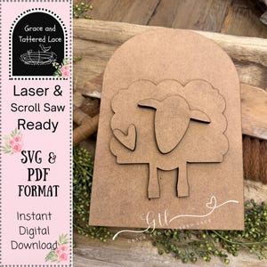 May include: A laser-cut wooden sheep design with a heart, set against a light brown background. The design is part of a larger wooden cutout with the text "Laser & Scroll Saw Ready" and "SVG & PDF FORMAT". The logo "Grace and Tattered Lace" is also visible.