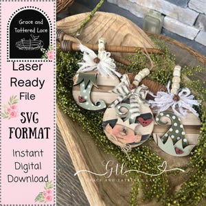 May include: Three wooden Christmas ornaments with elf hat and shoe designs, accented with bows and beads. The ornaments are set on a bed of greenery inside a wooden bowl. The image also includes text that says "Laser Ready File SVG Format Instant Digital Download."