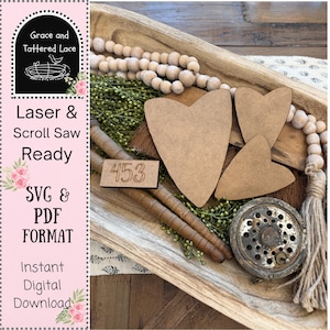 May include: A wooden tray holds three heart-shaped cutouts, a small rectangular sign with the number 453, and a vintage fishing reel. The tray also contains wooden beads, greenery, and two wooden dowels. Text on the left side reads "Grace and Tattered Lace" and "Laser & Scroll Saw Ready."