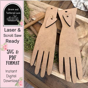 May include: Two wooden hand-shaped cutouts with heart accents. The cutouts are light brown with black edges and have a hole at the top. The image also includes text that reads "Grace and Tattered Lace", "Laser & Scroll Saw Ready", "SVG & PDF FORMAT", and "Instant Digital Download."