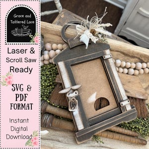 May include: A wooden lantern-shaped frame with a distressed finish, featuring a rectangular opening and a handle. The frame is adorned with decorative elements, including a small bird and a heart-shaped tag. The text "Laser & Scroll Saw Ready" and "SVG & PDF FORMAT" are visible.