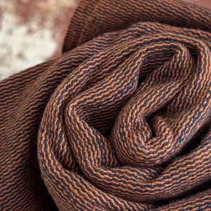 May include: A tightly rolled piece of fabric featuring a distinct woven texture with alternating thin stripes of dark brown and black. The material displays a consistent ribbed pattern throughout its surface, showing the dense weave of the textile.