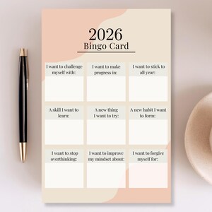 Op de afbeelding: Een beige en perzik 2026 Bingokaart met prompts voor zelfverbetering. De kaart bevat prompts zoals "Ik wil mezelf uitdagen met:" en "Een vaardigheid die ik wil leren:". Links staat een zwarte pen met gouden accenten.