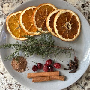 Könnte beinhalten: Ein Teller mit getrockneten Orangenscheiben, Zimtstangen, Preiselbeeren, Nelken und einem Zweig immergrünen. Diese Zutaten werden häufig verwendet, um Potpourri oder köchelndes Potpourri herzustellen.