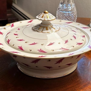May include: A white porcelain serving dish with a lid. The dish has a pink and gold floral pattern. The lid has a gold knob.